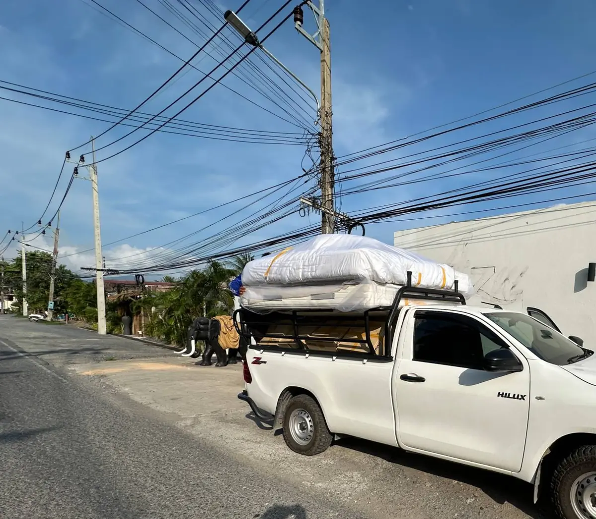 A loaded Hive pickup truck with a mattress and boxes strapped to the rack, on a road in Koh Samui